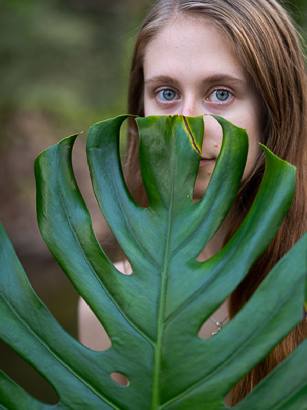 woman with beautiful eyes peaking over large green leaf